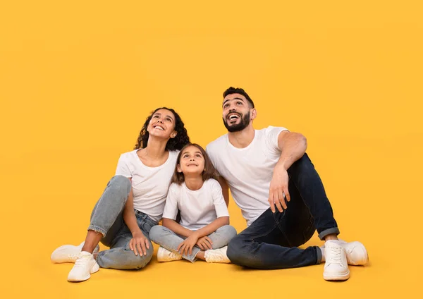 Família árabe positiva sentada olhando para cima posando sobre fundo amarelo — Fotografia de Stock