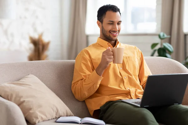 Lächelnder arabischer Mann schaut Video am Computer, trinkt Kaffee — Stockfoto