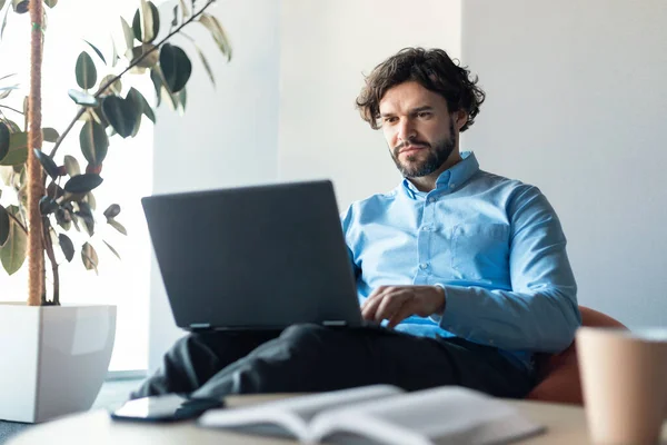 Zakenman met behulp van laptop zitten op boon zak in het kantoor — Stockfoto