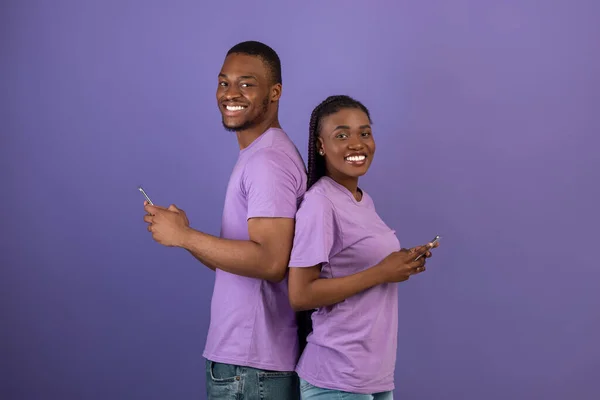Casal afro-americano usando smartphones, parede de estúdio violeta — Fotografia de Stock