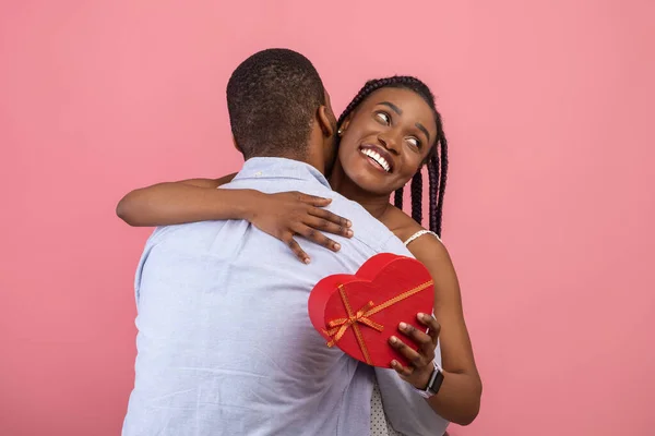 Hombre negro haciendo sorpresa para mujer dando caja, pareja abrazando — Foto de Stock