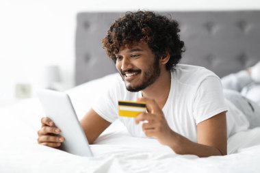 Gülümseyen Hintli adam dijital tablet ve kredi kartı kullanıyor.