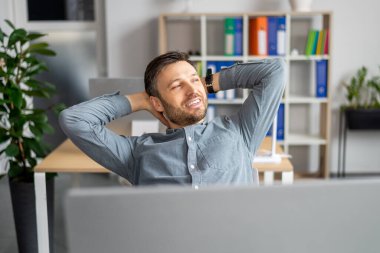 Successful businessman. Relaxed mature man holding hands behind head, sitting at desk in modern office