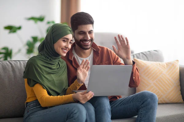 Casal islâmico fazendo chamada de vídeo acenando com as mãos para laptop interior — Fotografia de Stock