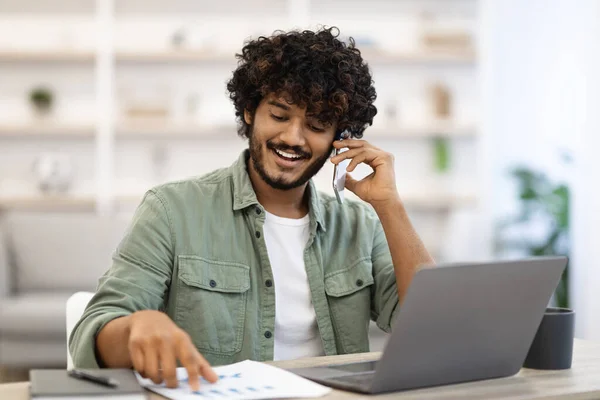 Positive handsome indian guy working online, having phone conversation — Stock Fotó