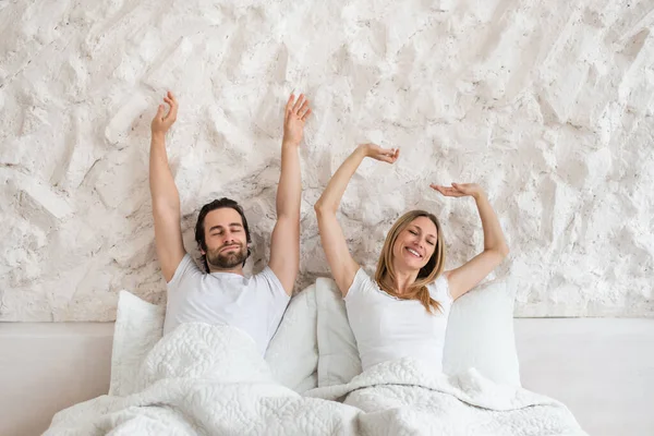 Счастливая миллениальная пара растягивается на кровати после пробуждения, чувствует сонливость дома, копировать пространство — стоковое фото
