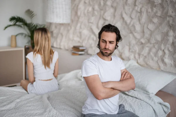 Unhappy young couple having relationship problems, sitting on opposite sides of bed, not looking at each other at home — Stockfoto