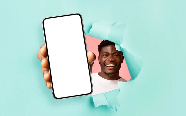 Чорний хлопець показує білий порожній екран смартфона через рваний папір — стокове фото