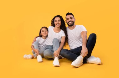 Middle Eastern Parents And Daughter Embracing Sitting On Yellow Background