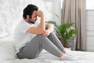 Unhappy millennial man feeling down, bedroom interior