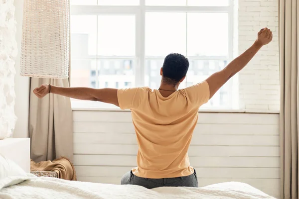 Man Sitting On Bed Stretching Arms In Bedroom, Back View — Stock Photo, Image