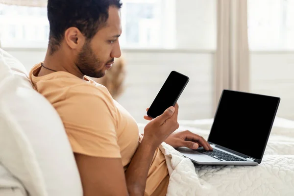 Man Using Phone And Laptop Sitting In Bed At Home —  Fotos de Stock