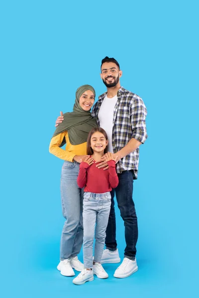 Tiro vertical de família muçulmana abraçando de pé sobre fundo azul — Fotografia de Stock