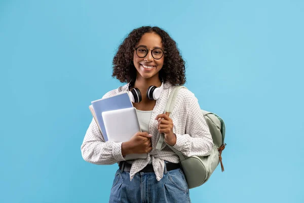 Online education. Smiling black female student with backpack and headphones holding notebooks and digital tablet — Foto Stock