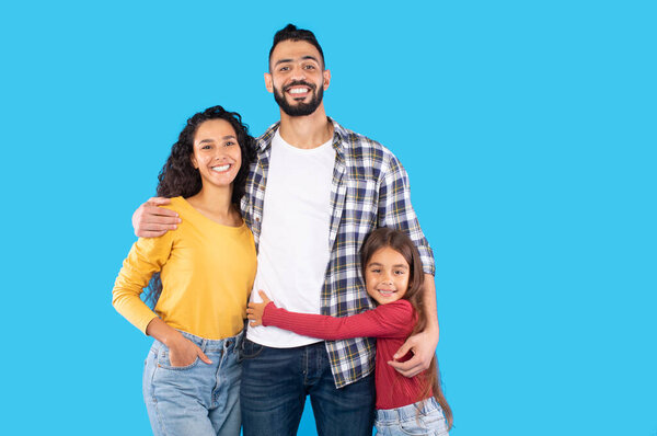Positive Parents And Daughter Posing Together Hugging On Blue Background