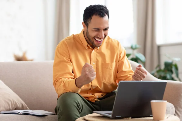 Uomo arabo utilizzando il computer portatile che celebra il successo scuotendo pugni urlando sì — Foto Stock