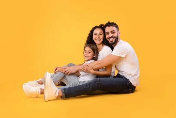 Família árabe de três abraçando juntos sentados sobre fundo amarelo — Fotografia de Stock