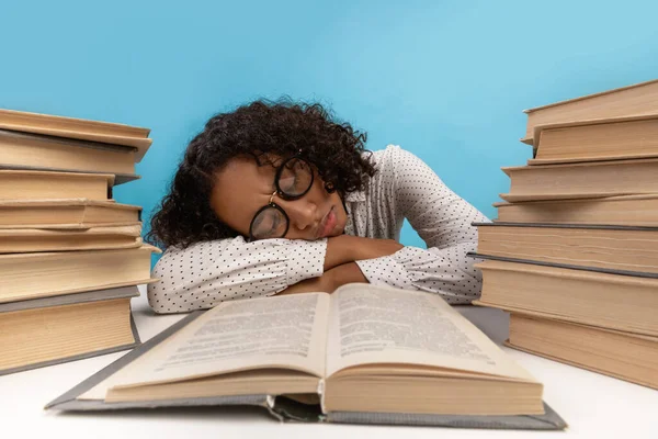 Exhausted African American female student sleeping on desk among stacks of books, being tired while preparing for exam — Fotografia de Stock