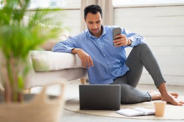 Evde akıllı telefon ve bilgisayar kullanan odaklanmış bir adamın portresi