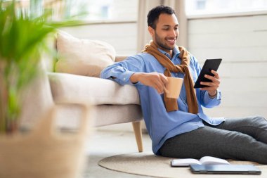 Gülümseyen Arap adam tabletten video izliyor, kahve içiyor.