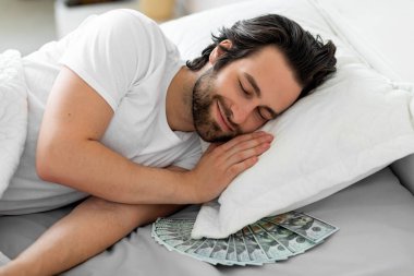 Gülümseyen sakallı adam yastığının altında parayla uyuyor.