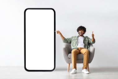 Handome young indian man pointing at huge smartphone, mockup