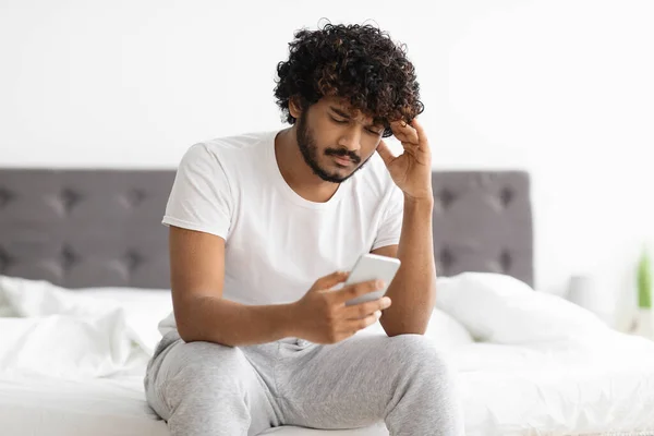 Confused indian guy looking at smartphone screen and touching head — Foto de Stock