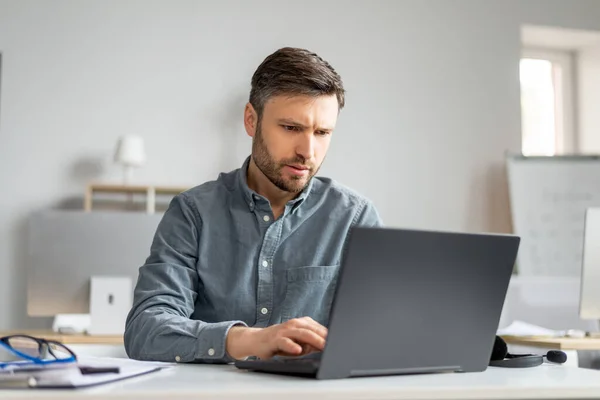 Gerente masculino maduro trabajando en el ordenador portátil en la oficina moderna, sentado en la mesa, escribiendo en el teclado de la computadora — Foto de Stock