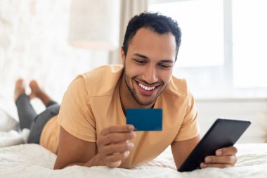 Yatak odasında dijital tablet kullanan mutlu Arapça adam çevrimiçi alışveriş yapıyor