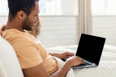Middle Eastern Man Using Laptop With Empty Screen In Bedroom