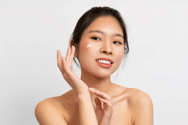 Portrait of Asian woman touching applying cream on cheek — Foto de Stock