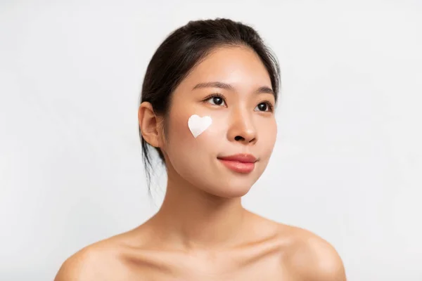 Asiatico ragazza posa con cuore a forma di crema sulla guancia — Foto Stock