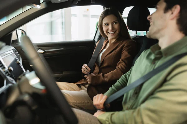 Glada unga par sitter i bilsalong, nöjd med provkörning, diskuterar inköp av ny bil hos bilhandlare — Stockfoto