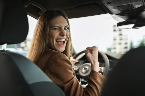 Jovem excitada celebrando a compra bem sucedida do carro, gesticulando SIM enquanto se senta dentro do salão de auto na concessionária — Fotografia de Stock