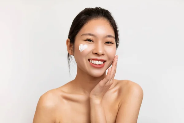 Asiatisk kvinna poserar med hjärtformad kräm på kinden — Stockfoto