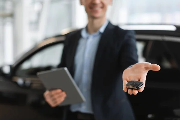 Cropped view of young salesman showing car key in modern dealership, selective focus. Vehicle local distribution — 스톡 사진