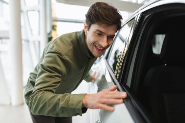 Yakışıklı genç adam yeni arabayı kontrol ediyor, araba galerisinden lüks bir araç alıyor.