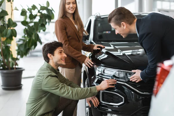 행복 한 젊은 부부가 판매원 과상의 하면서 자동차 판매점에서 새 차를 선택 한다 — 스톡 사진