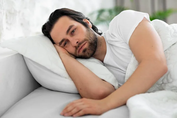 Depressed man laying in bed alone, looking at copy space — Stock Fotó