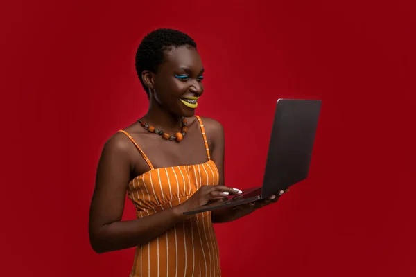 Веселая привлекательная черная женщина с помощью компьютера на красном — стоковое фото