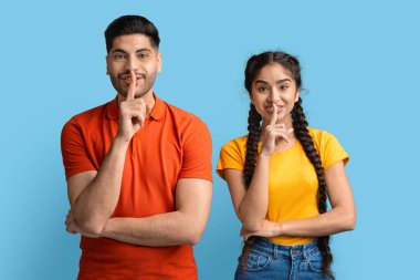 Neşeli Arap çift kameraya sessizlik işareti gösteriyor, parmaklarını dudaklarında tutuyorlar