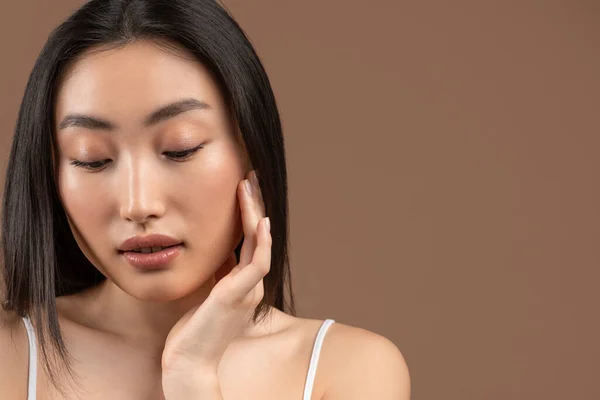 Natural skincare. Young pretty asian woman caressing her smooth soft skin, brown background, copy space — Stok fotoğraf