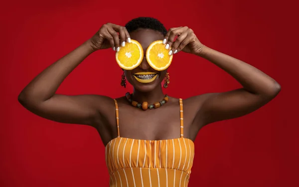Joyful black lady holding orange circles over her eyes — Stock Photo, Image