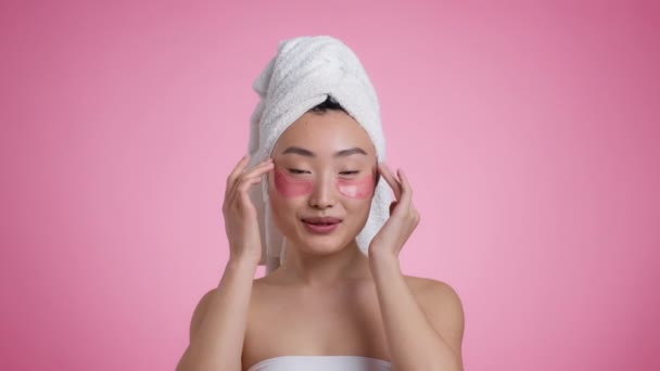 Morning beauty routine. Young peaceful asian lady with towel on head putting collagen anti edema patches under eyes — Vídeos de Stock