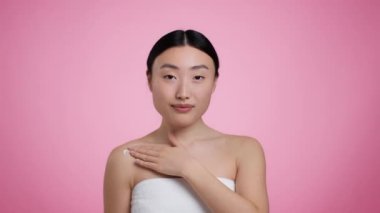 Duştan sonra vücut bakımı. Havluya sarılı genç Asyalı kadın omuzlarına krem sürüyor.