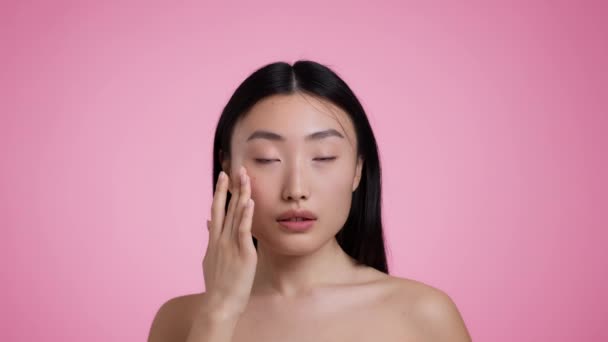 Skin vitamization. Young asian lady applying nourishing serum, smiling to camera, pink studio background, slow motion — Vídeos de Stock