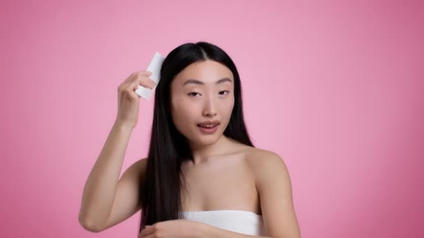 Hair care concept. Young asian woman combing hair with special brush, smiling over pink studio background, slow motion — Vídeos de Stock