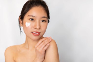 Yanağında kalp şeklinde krem olan Asyalı kadın.