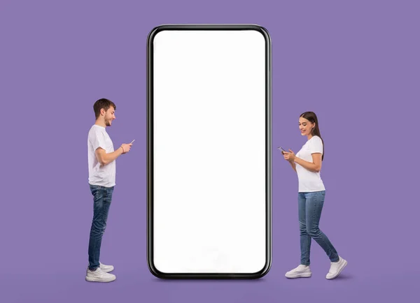 Couple standing near white empty smartphone screen and using phones — Stockfoto