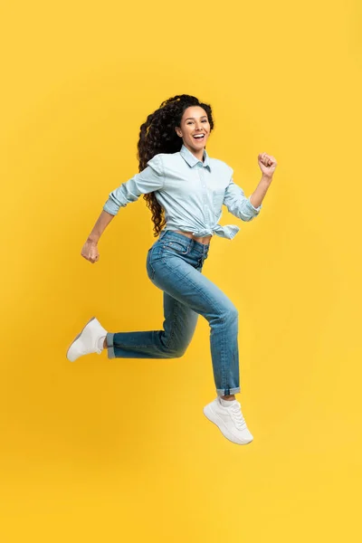 Spännande ung kvinna hoppar upp på orange studio — Stockfoto